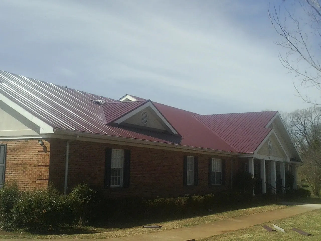 Red metal roof with gabled entries on a long brick building, from a Hail Damage Roof Repair job in Big Rock