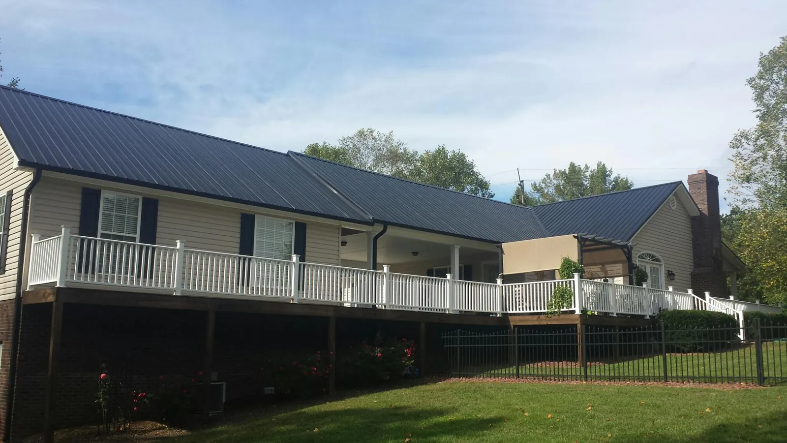 Black metal roof above a long white railed deck on a hillside home in Big Rock